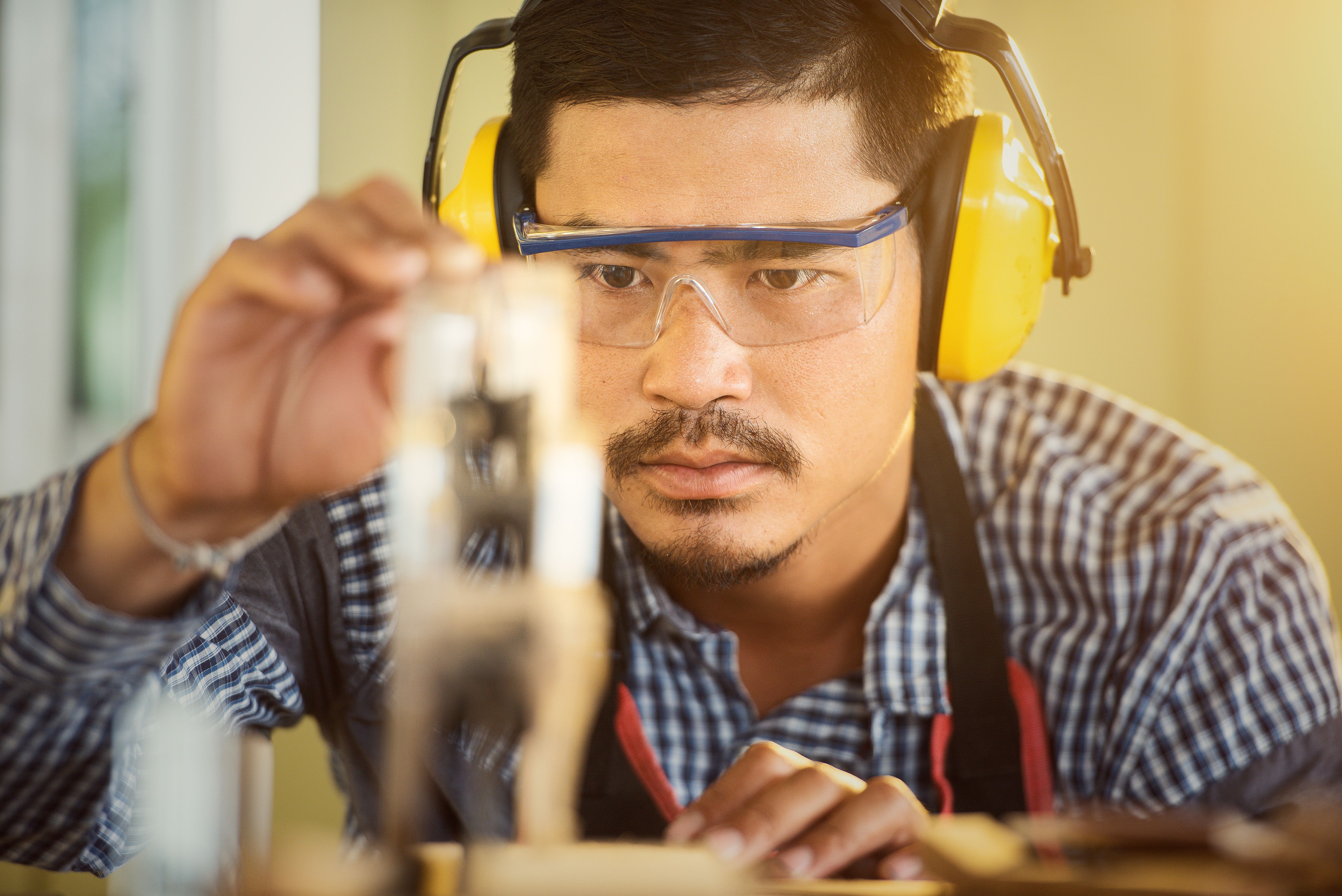 Carpenter wearing safety glasses and ear defenders checking timber in a workshop