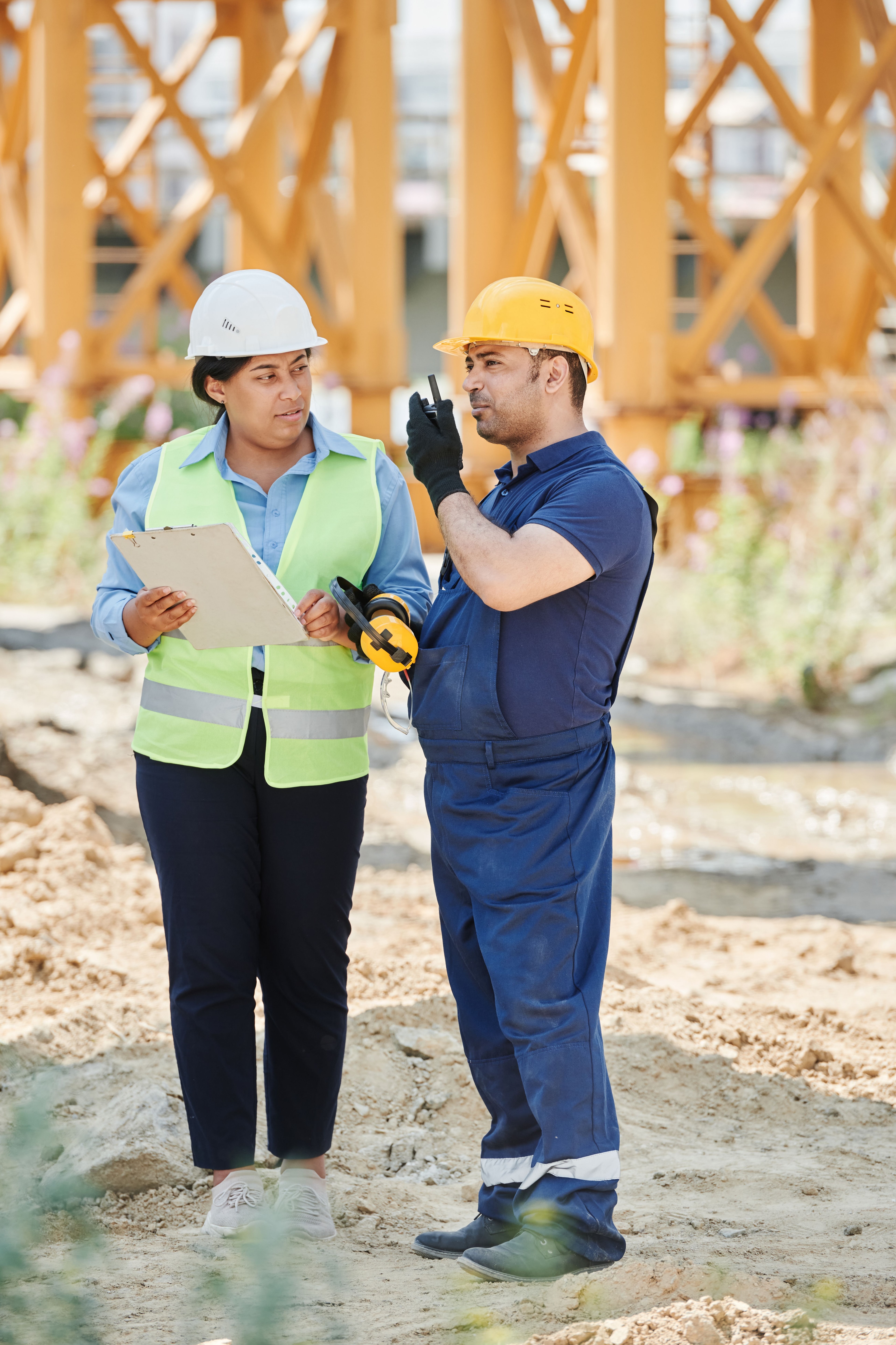 Two construction professionals in hard hats reviewing a site plan beside timber framing